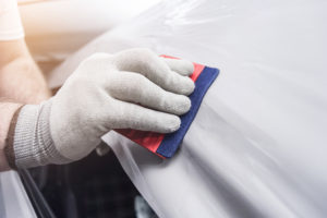 Auto technician cleaning a fresh paint job on a white car.