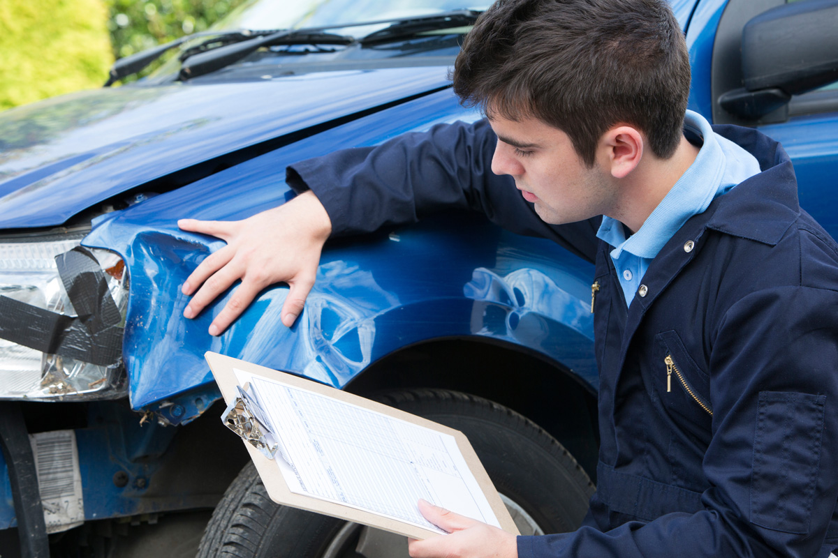 A person holding a clipboard inspecting a damaged blue car in El Paso.