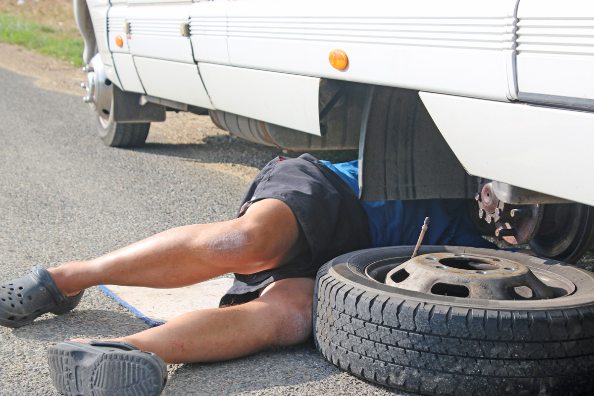 A person laying under an RV missing its tire performing maintenance in El Paso.