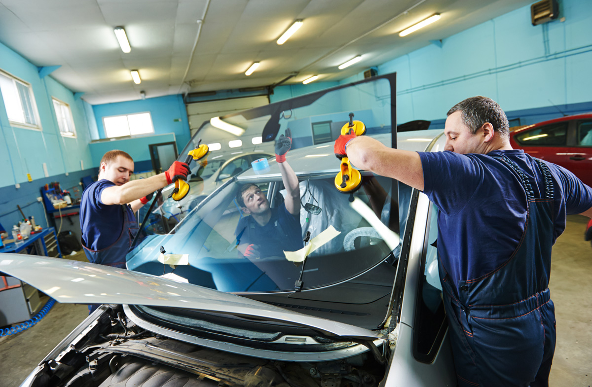 Two people performing auto glass repair at a body shop in El Paso.