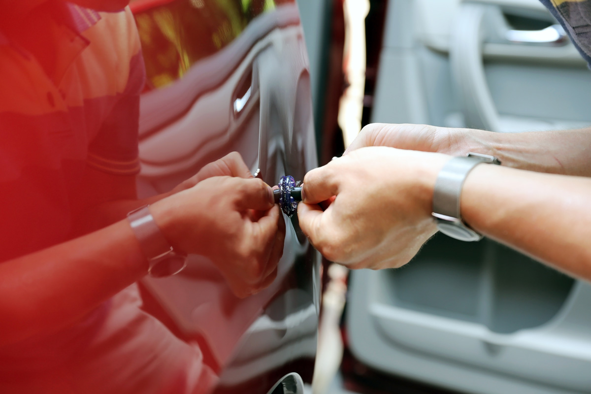 A person performing paintless dent repair on a red vehicle in El Paso.