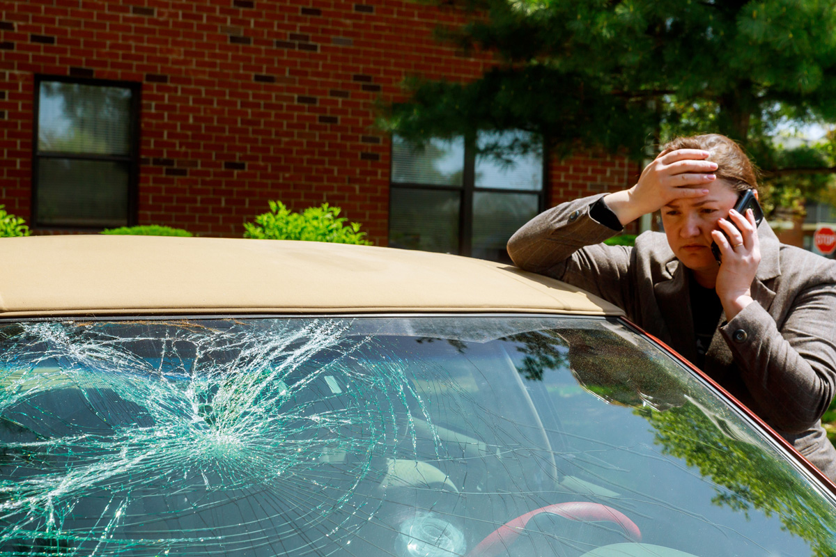 A woman on the phone looking at her car’s shattered windshield in El Paso.